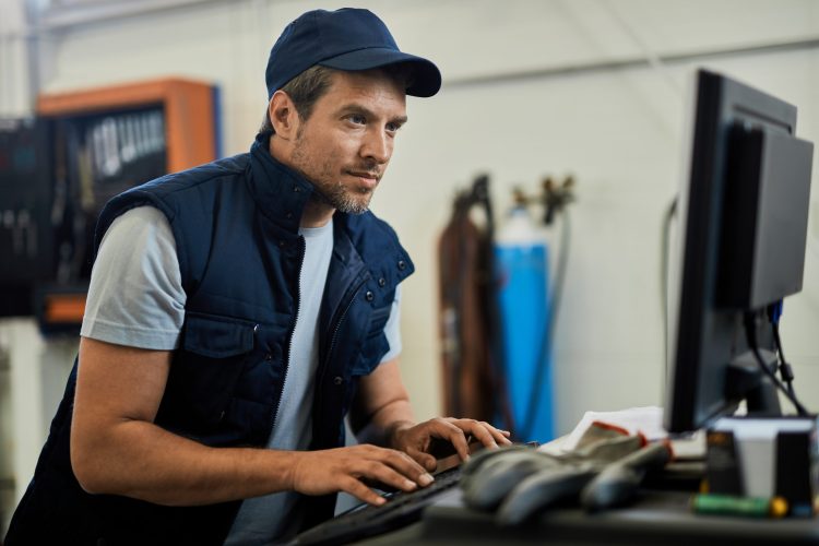 Auto repairman working on a computer in a workshop. Car mechanic using computer while working in auto repair shop.